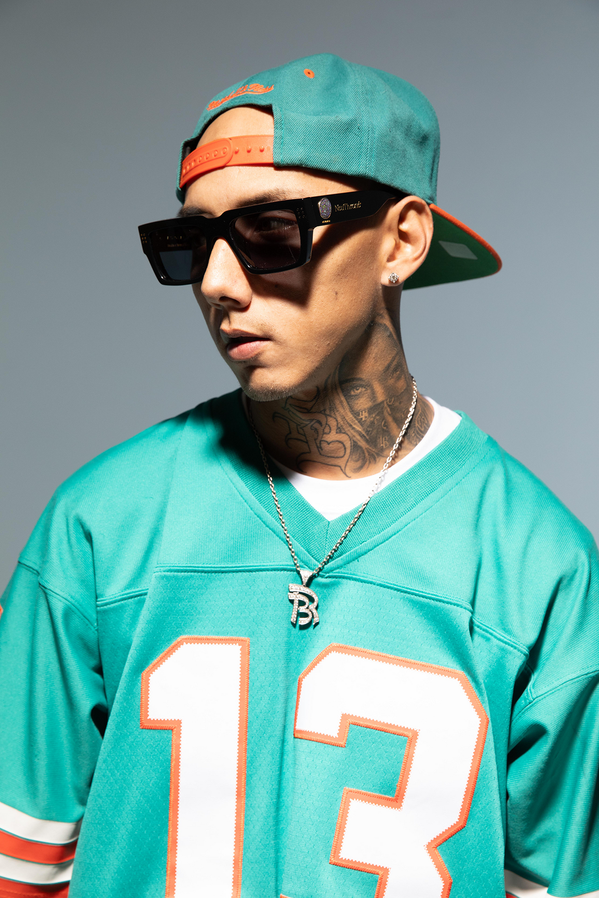 Person wearing a teal sports jersey with number 13 and a cap, on a gray background