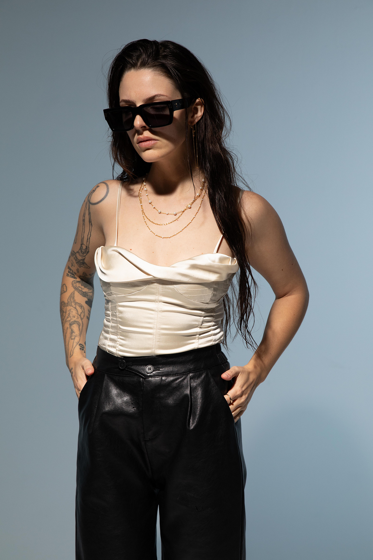 Woman wearing a white top and black pants with sunglasses against a gray background