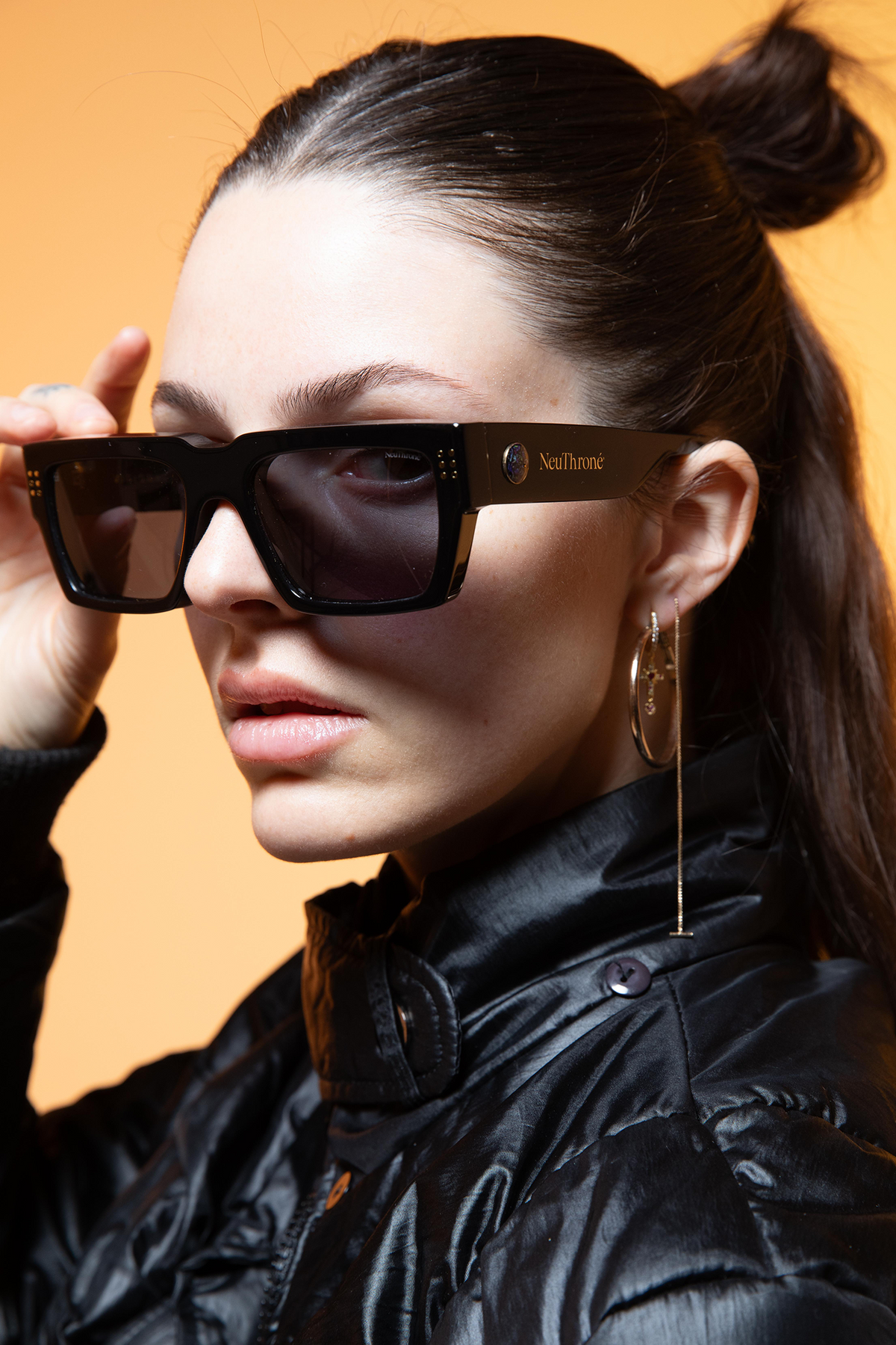 Woman wearing black sunglasses with a brand logo against an orange background